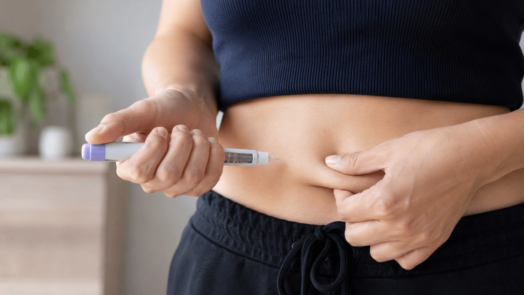 Person preparing to inject an unbranded weight loss injection pen into their stomach at home, with a close-up of hands and abdomen.