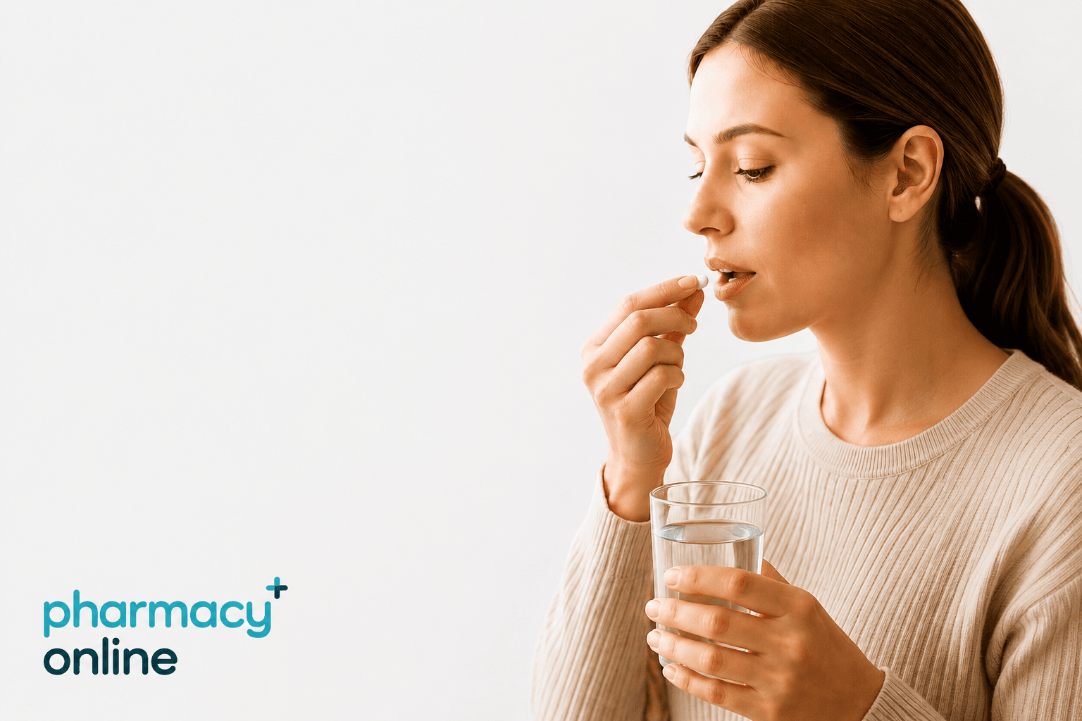 A woman holding a tablet to her mouth in one hand and a glass of water in the other as if getting ready to take a tablet